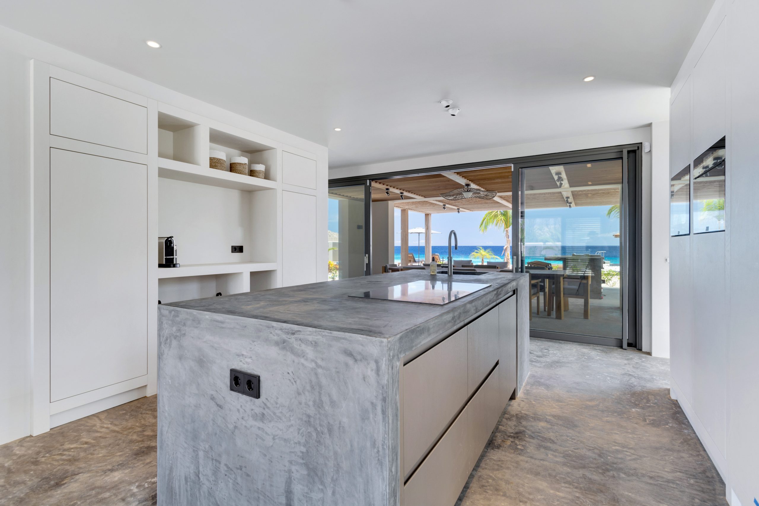 Maatwerkkeuken met doorlopende kastenwand en betonlook kookeiland in Villa Bonaire.